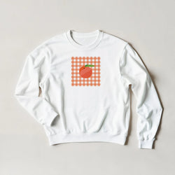 White sweatshirt with orange gingham square and peach graphic.