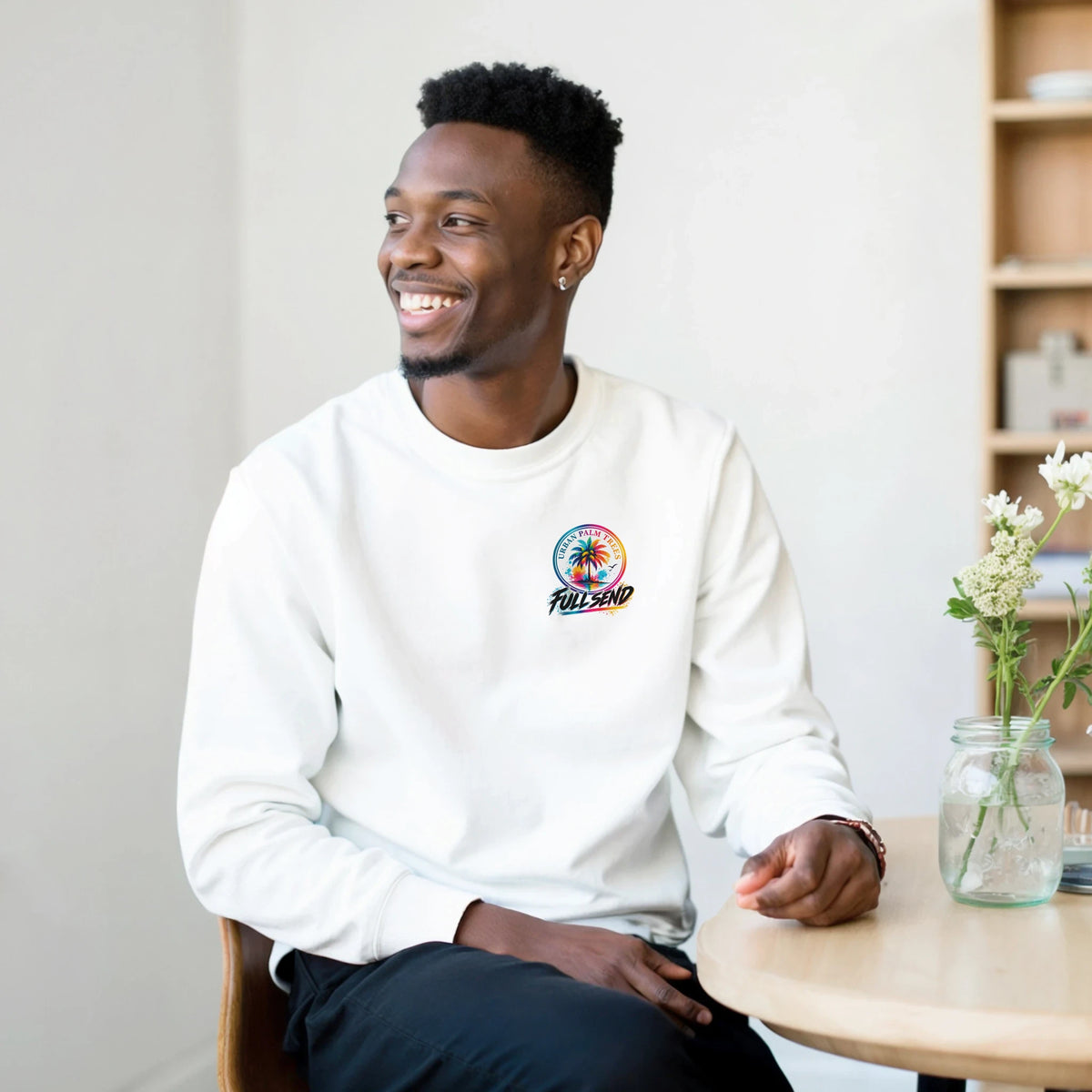 A man wearing a white Full Send Petrolhead sweatshirt featuring a colorful Urban Palm Trees logo on the chest.