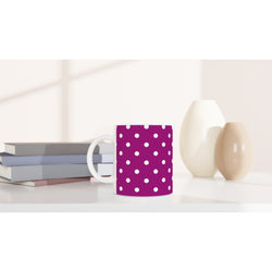 Retro purple ceramic mug with white polka dots sitting on a white desk beside stacked books and small vases.