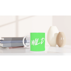 Cute Wild And Free mug with green body and white cursive slogan on a desk beside books and a lamp.