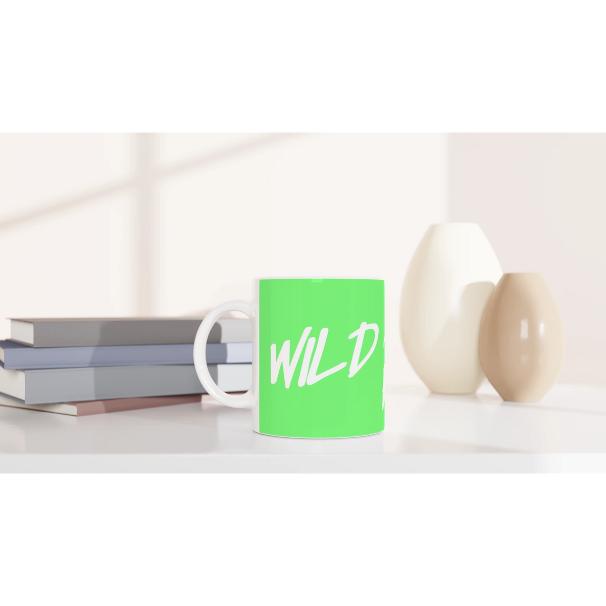 Cute Wild And Free mug with green body and white cursive slogan on a desk beside books and a lamp.