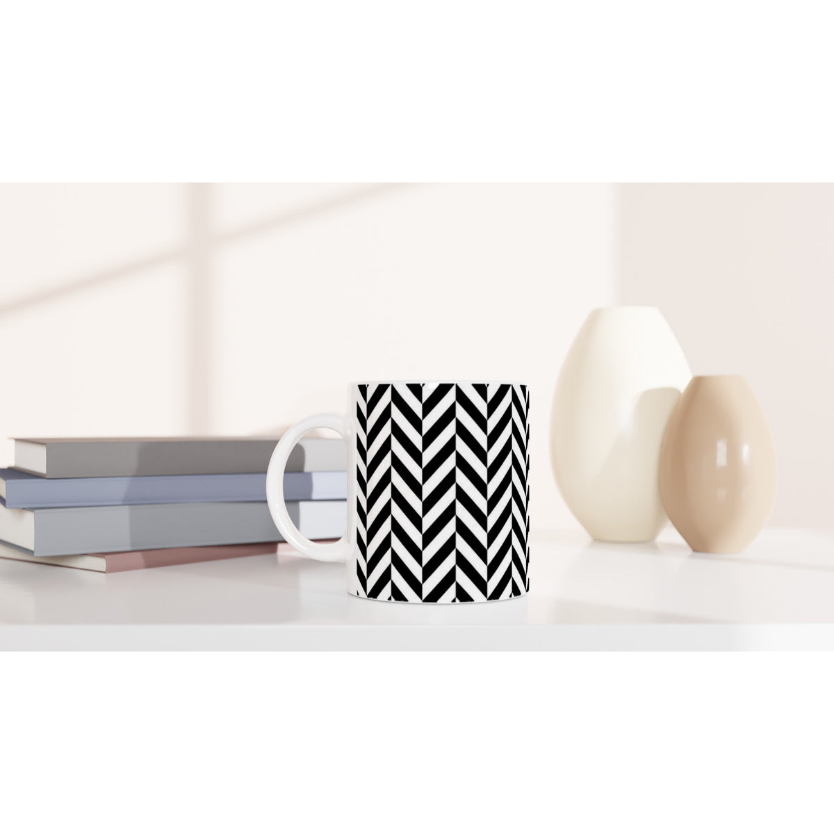 Black and white herringbone geometric ceramic coffee mug on a white desk with books and decorative vases.