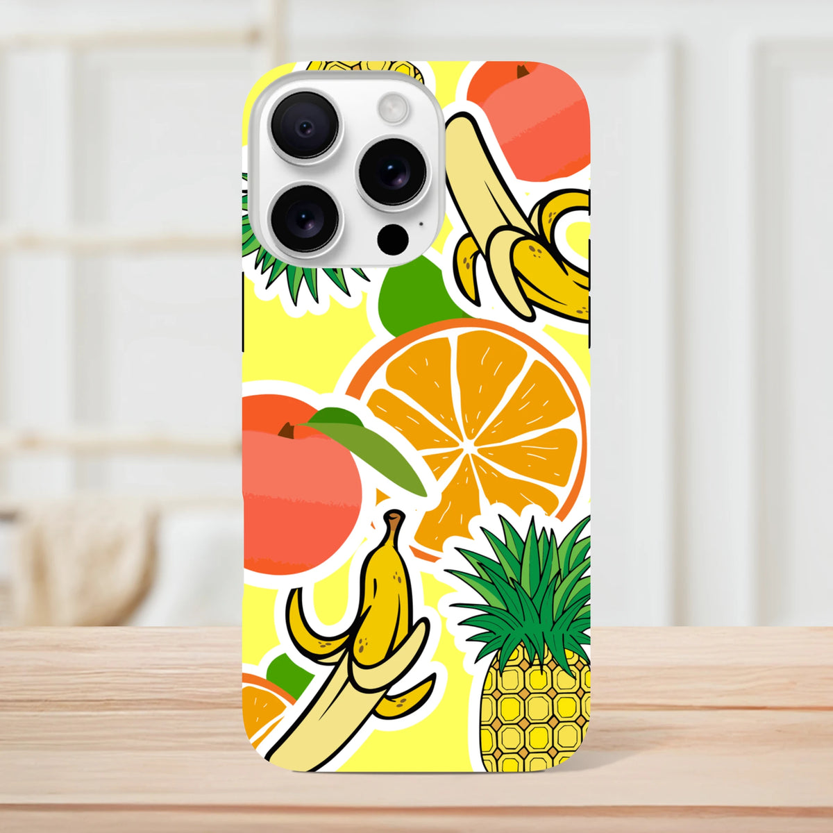 Yellow iPhone case featuring bold sticker-style graphics of oranges, bananas, pineapples, and peaches on a bright background.