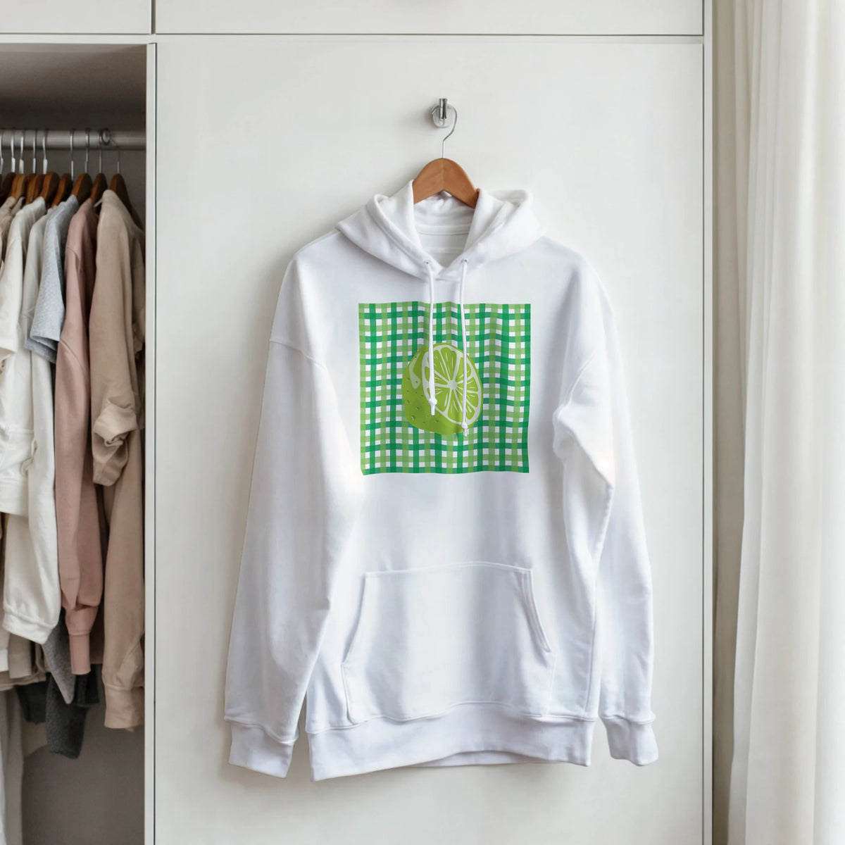 White hoodie featuring a retro lime gingham graphic and kangaroo pocket, hanging on a wooden hanger in a closet.