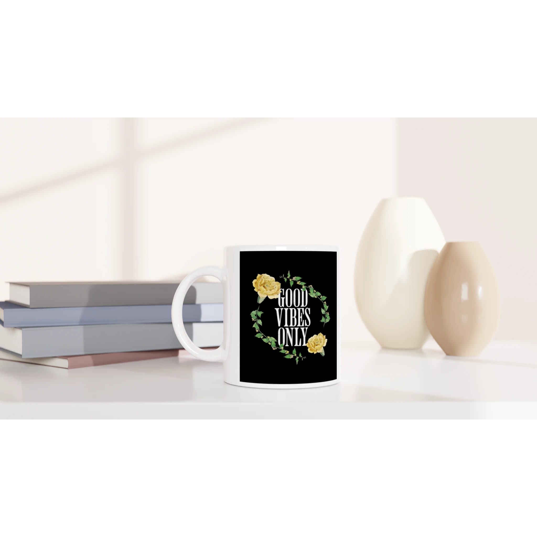 White ceramic mug with Good Vibes Only floral wreath on black, on a shelf beside books and vases.