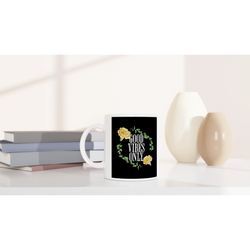 White ceramic mug with Good Vibes Only floral wreath on black, on a shelf beside books and vases.