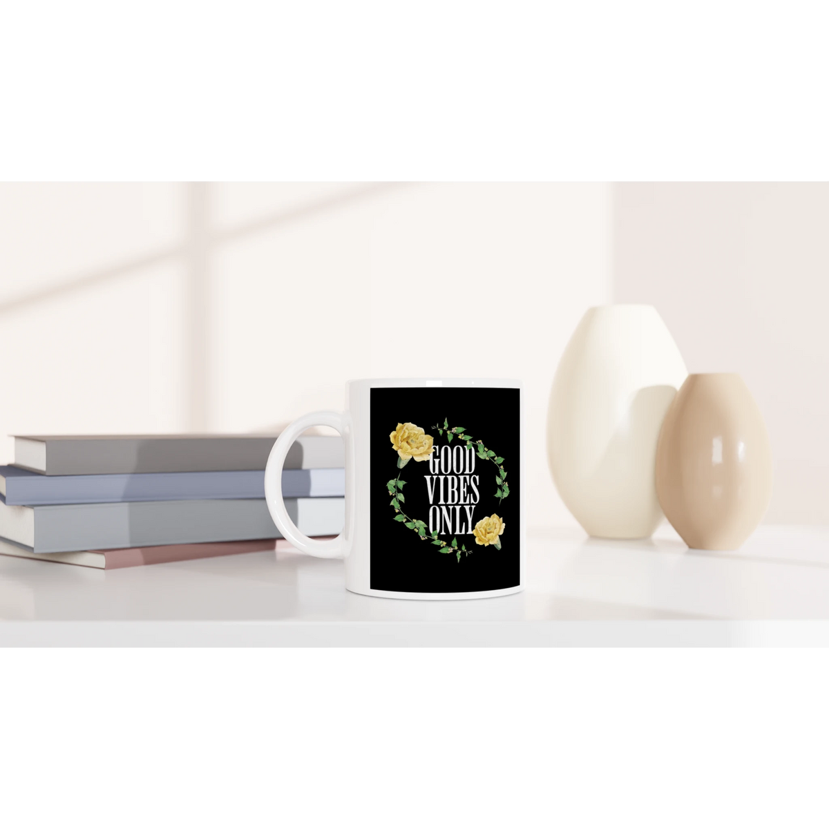 White ceramic mug with Good Vibes Only floral wreath on black, on a shelf beside books and vases.