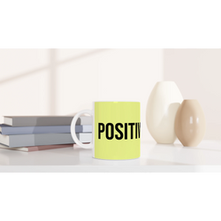 Lime-green mug with bold POSITIVE slogan on a white desk next to books.