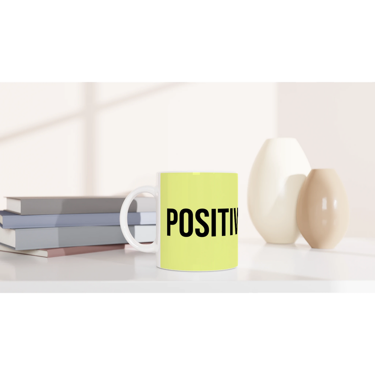 Lime-green mug with bold POSITIVE slogan on a white desk next to books.