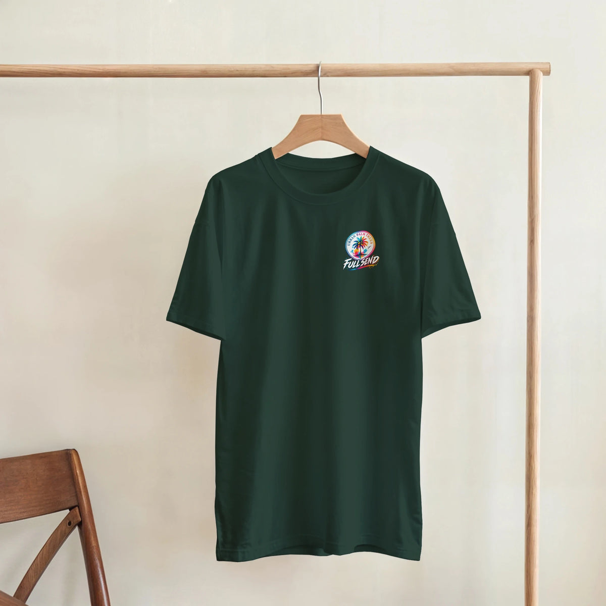 Dark green graphic tee with colorful palm tree "Full Send" logo hanging on wooden rack, perfect for modified car culture streetwear.