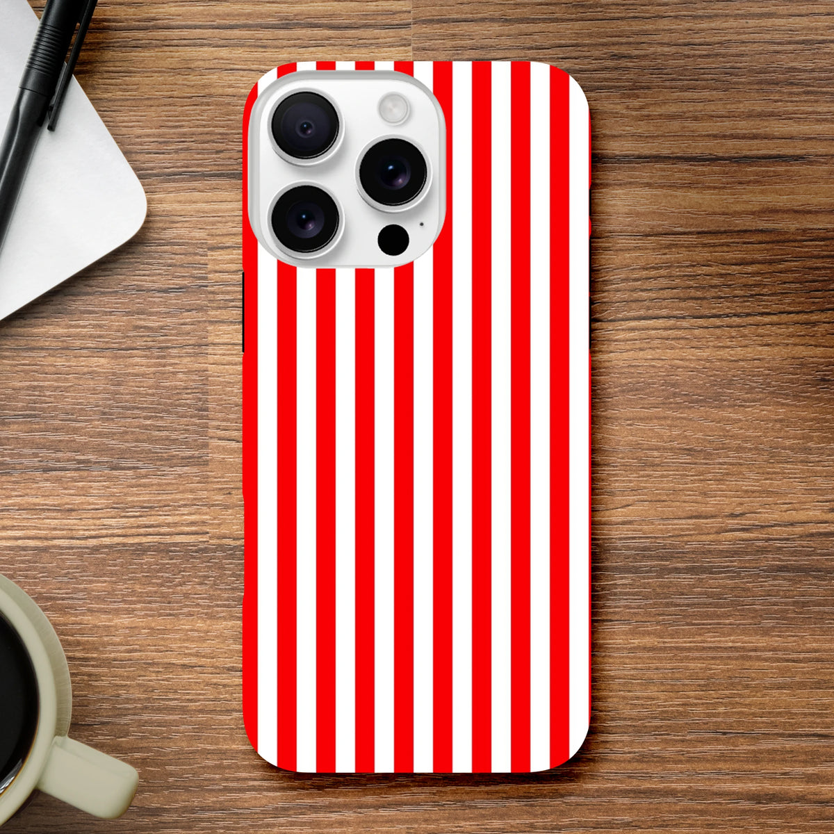 Retro red and white vertical striped tough iPhone case on wooden desk with pen and coffee cup.