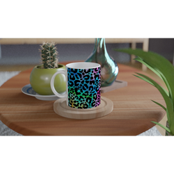 Rainbow leopard-print coffee mug on a wooden table beside a cactus and greenery.
