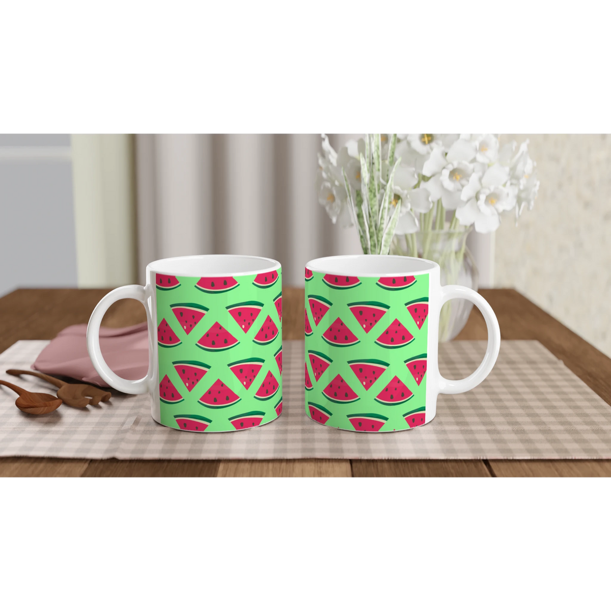 Two ceramic mugs featuring a cute pattern of red watermelon slices on a bright green background, set on a checkered placemat.