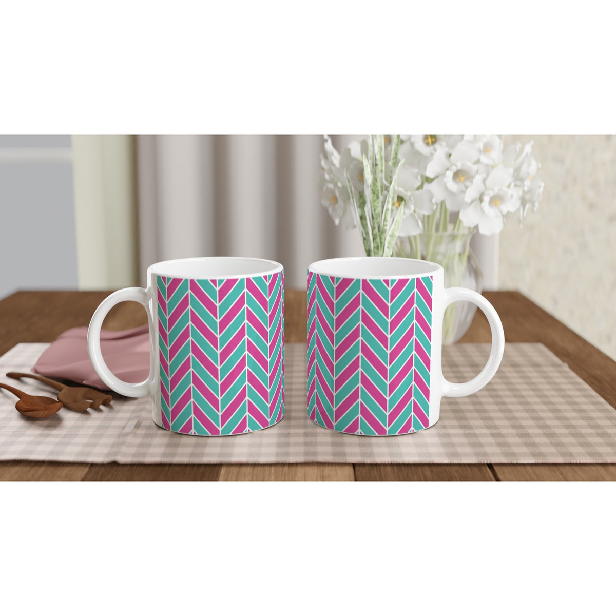 Two glossy ceramic mugs featuring a retro pink and aqua herringbone geometric pattern sitting on a checkered placemat.
