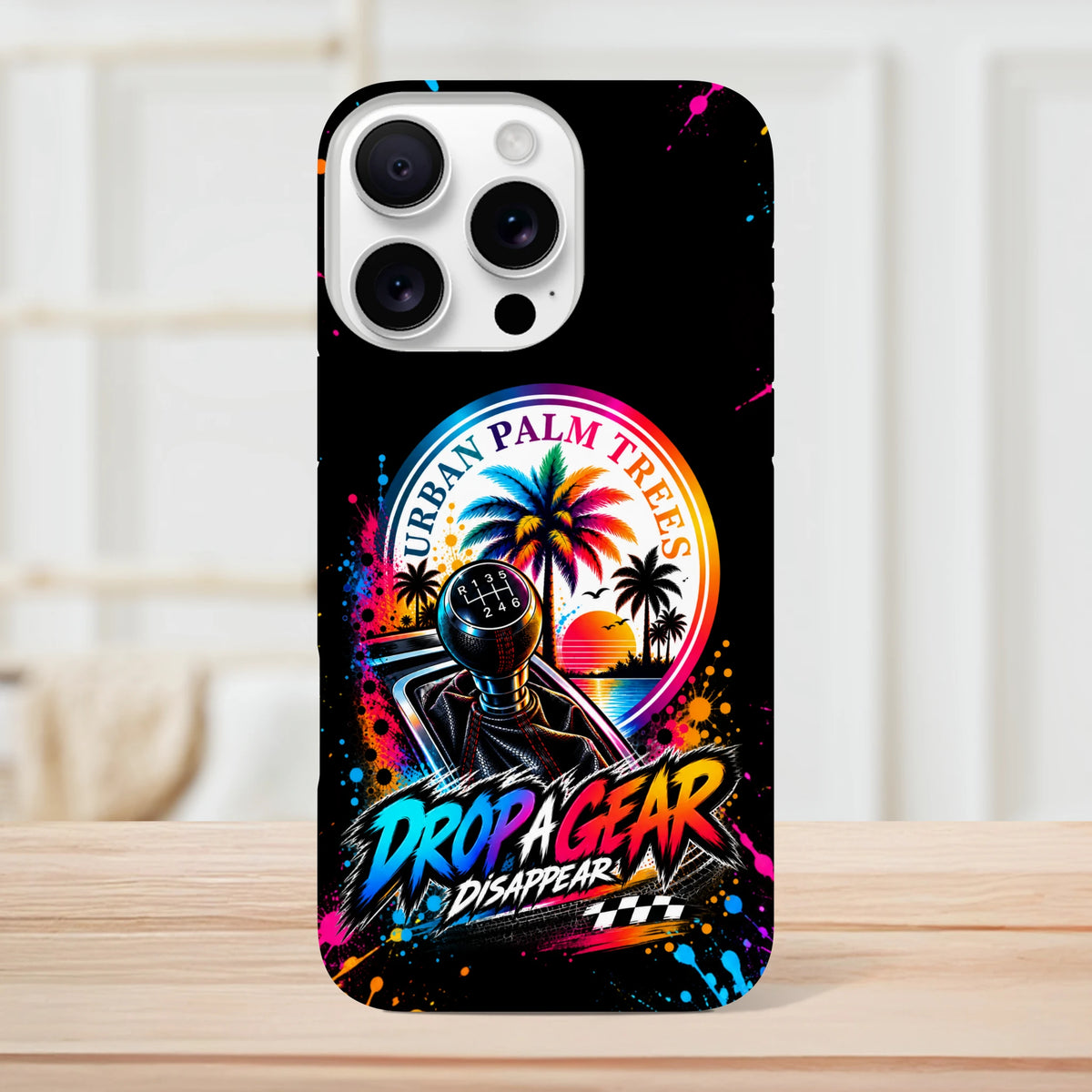 Black iPhone case featuring a colorful manual gear shifter, "Urban Palm Trees" sunset graphic, and "Drop A Gear" text with paint splatters.