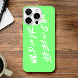 Bright green iPhone case featuring vertical white "Wild and Free" script text, embodying a bold Y2K aesthetic slogan on a wooden surface.