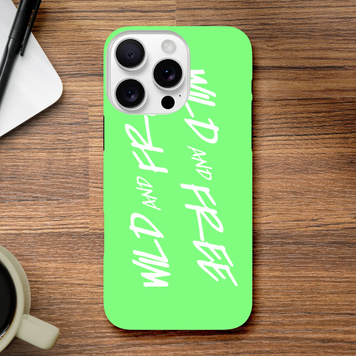 Bright green iPhone case featuring vertical white "Wild and Free" script text, embodying a bold Y2K aesthetic slogan on a wooden surface.