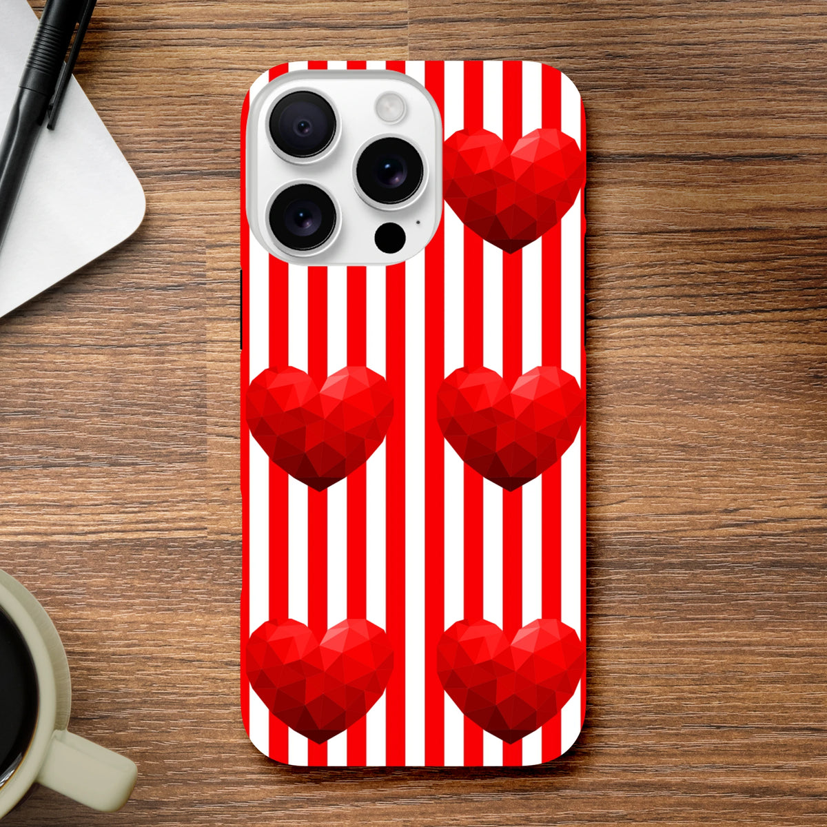 Red and white vertical striped iPhone case featuring five faceted 3D red hearts on a wooden desk.