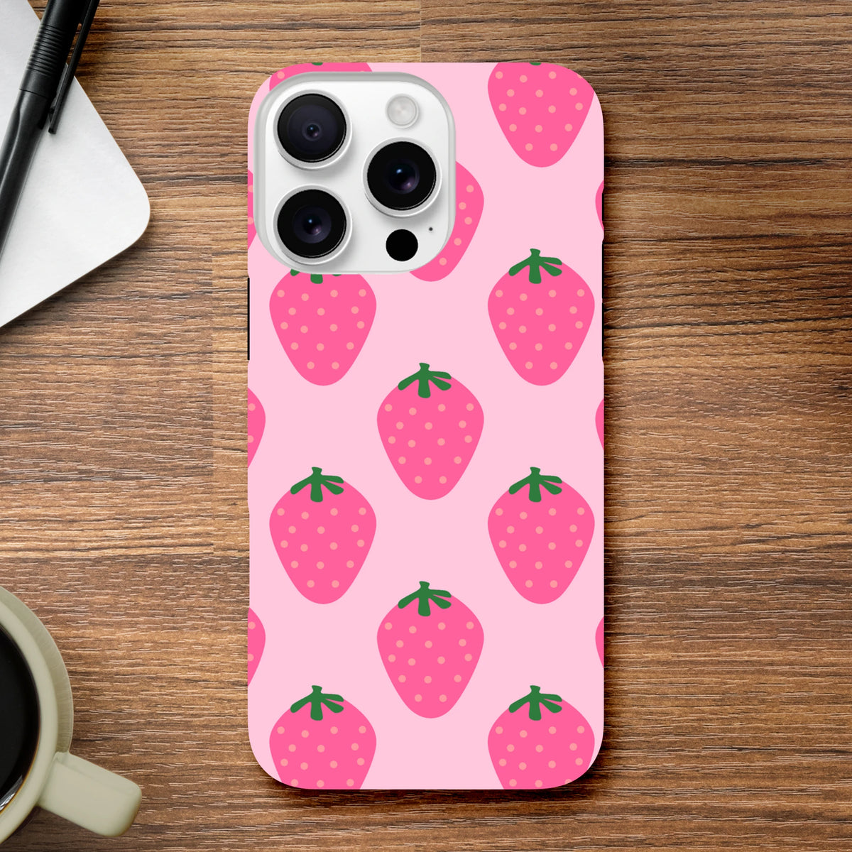 Pink strawberry pattern iPhone case with cute fruit design and high-gloss finish on wooden desk.