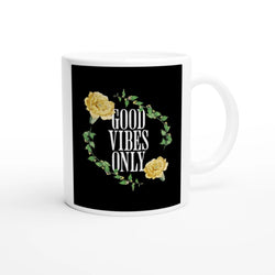 White ceramic mug with a black panel featuring circular wreath of green leaves and yellow roses around GOOD VIBES ONLY.
