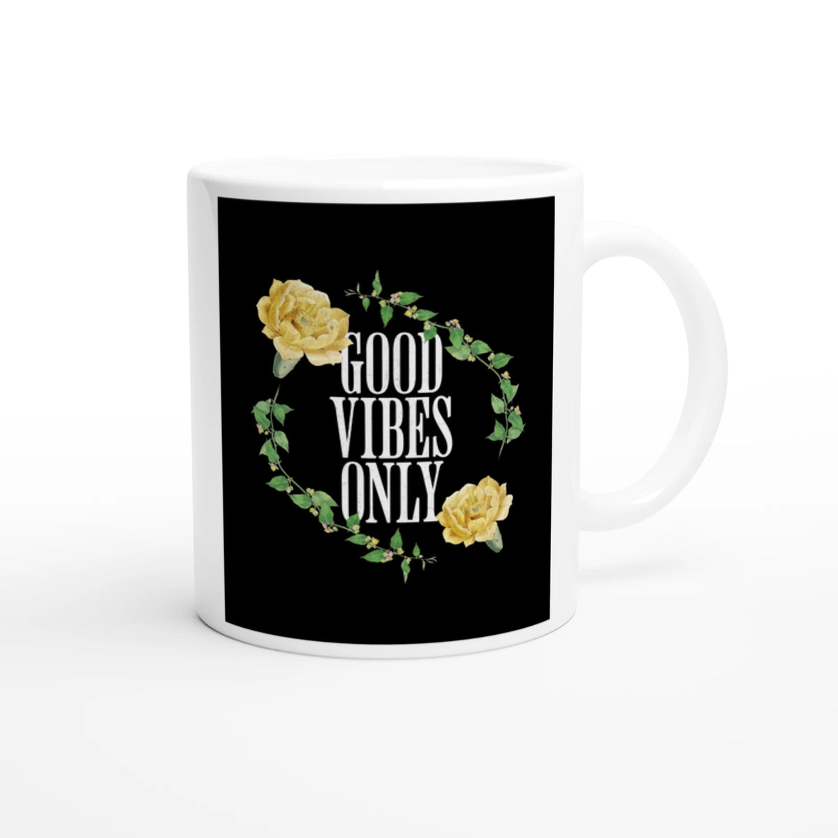 White ceramic mug with a black panel featuring circular wreath of green leaves and yellow roses around GOOD VIBES ONLY.