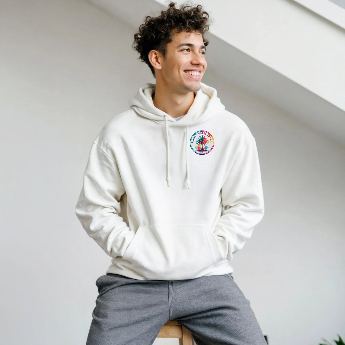 Man wearing white hoodie with colorful Urban Palm Trees chest logo. Retro graphic streetwear for men featuring vibrant palm tree design.