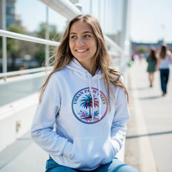 Woman wearing light-blue Urban Palm Trees Hoodie with palm graphic, hood and front pocket outdoors.