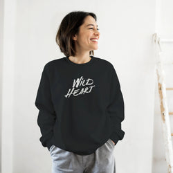 Smiling woman wearing a black Cute Wild Heart sweatshirt with a bold white slogan.