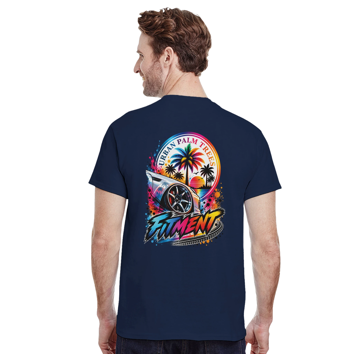 Man wearing navy blue Fitment Petrolhead graphic tee featuring a modified car, palm trees, sunset, and colorful splatter art on the back.