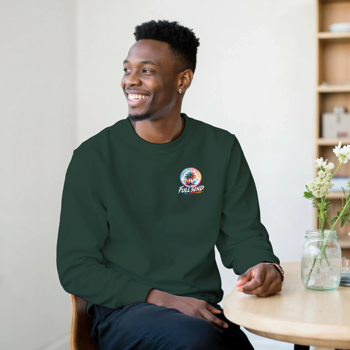 Man wearing dark green graphic jumper featuring a colorful Urban Palm Trees Full Send logo on the chest.