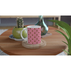 Retro pink and brown polka dot ceramic coffee mug on a wooden coaster beside a small cactus.