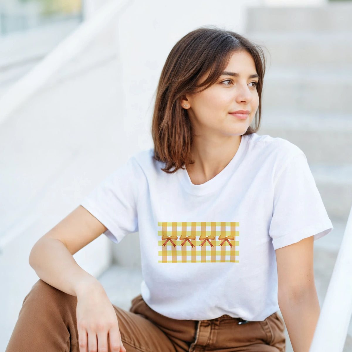 Woman wearing white T-shirt with yellow gingham bow print, Coquette aesthetic.