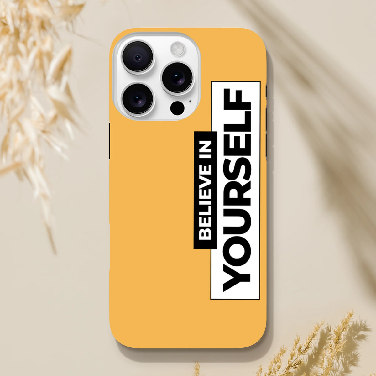 Orange tough iPhone case featuring bold vertical "BELIEVE IN YOURSELF" slogan text in high-contrast black and white blocks.