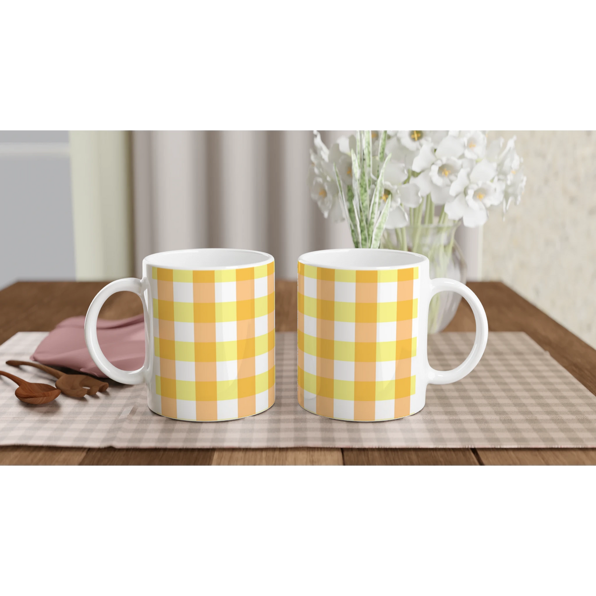 Yellow gingham ceramic mugs on a wooden table with a vase of white flowers.