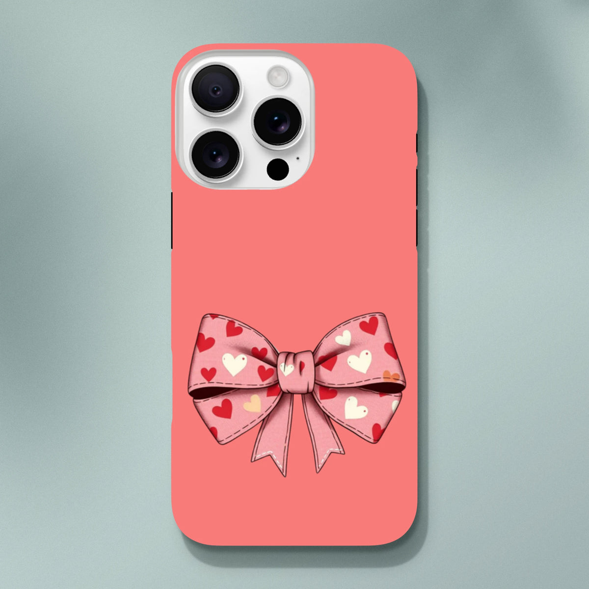 Pink iPhone case with a large bow patterned with red and white hearts on a coral background. Cute coquette tough phone cover.