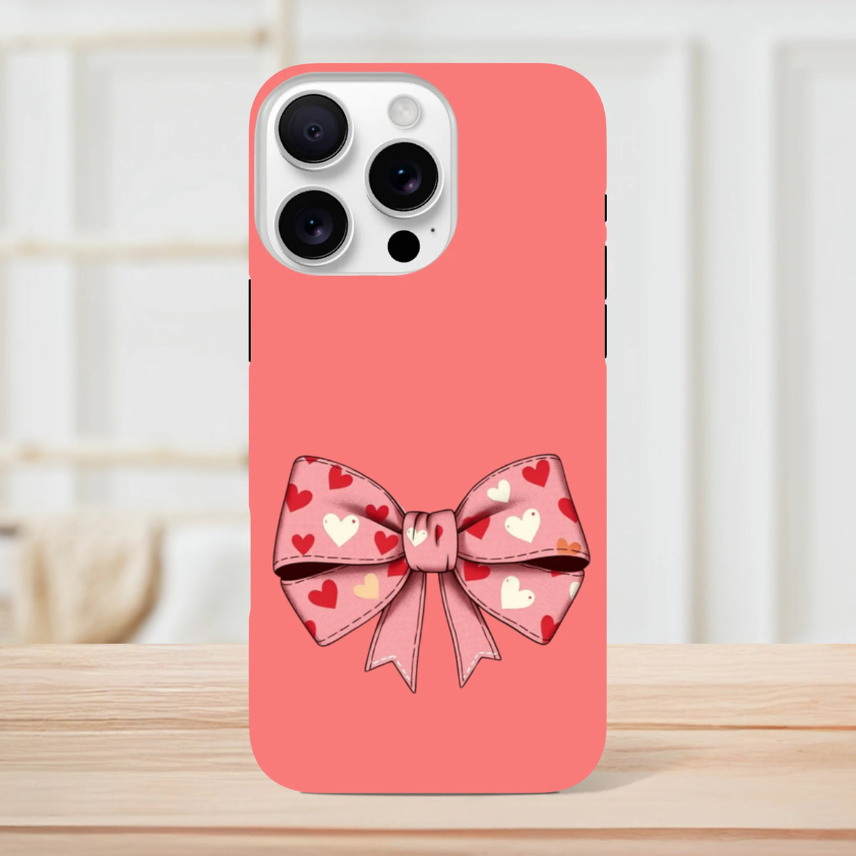 Pink tough iPhone case featuring a cute coquette bow graphic with red and white hearts on a coral background.