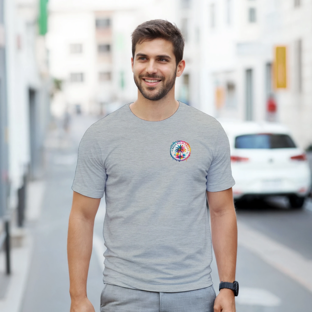 Man wearing grey t-shirt with colorful circular Urban Palm Trees logo on chest while walking down a city street.