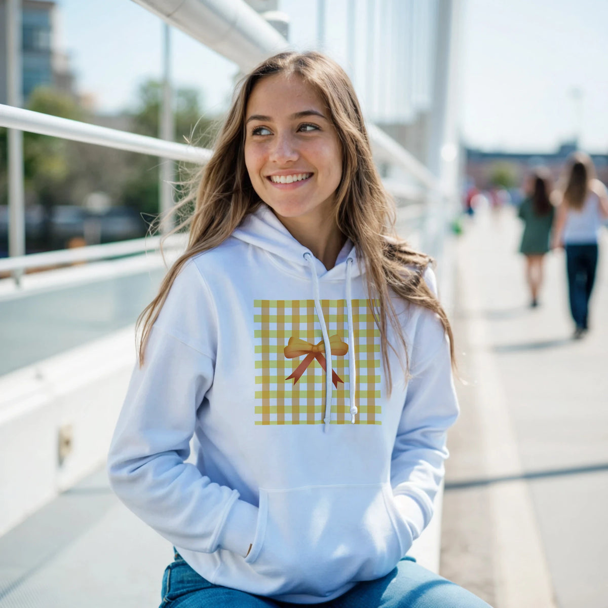 Smiling woman wearing a light-blue hoodie with a yellow gingham bow graphic, a Coquette aesthetic jumper.