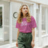 Woman wearing Cute Wild And Free T-Shirt with retro slogan on pink tee, urban street backdrop.