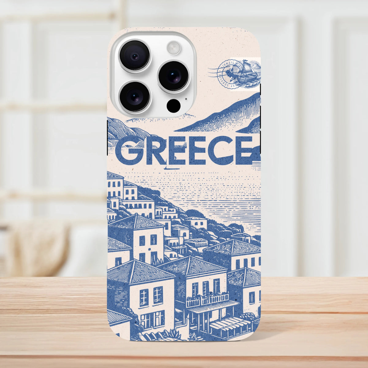 Vintage Greece iPhone case featuring a blue and cream Mediterranean village illustration, bold "GREECE" text, and an airmail stamp design.