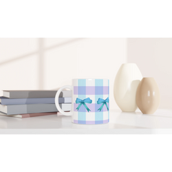 Blue gingham bow mug with teal bows on a white desk beside books.