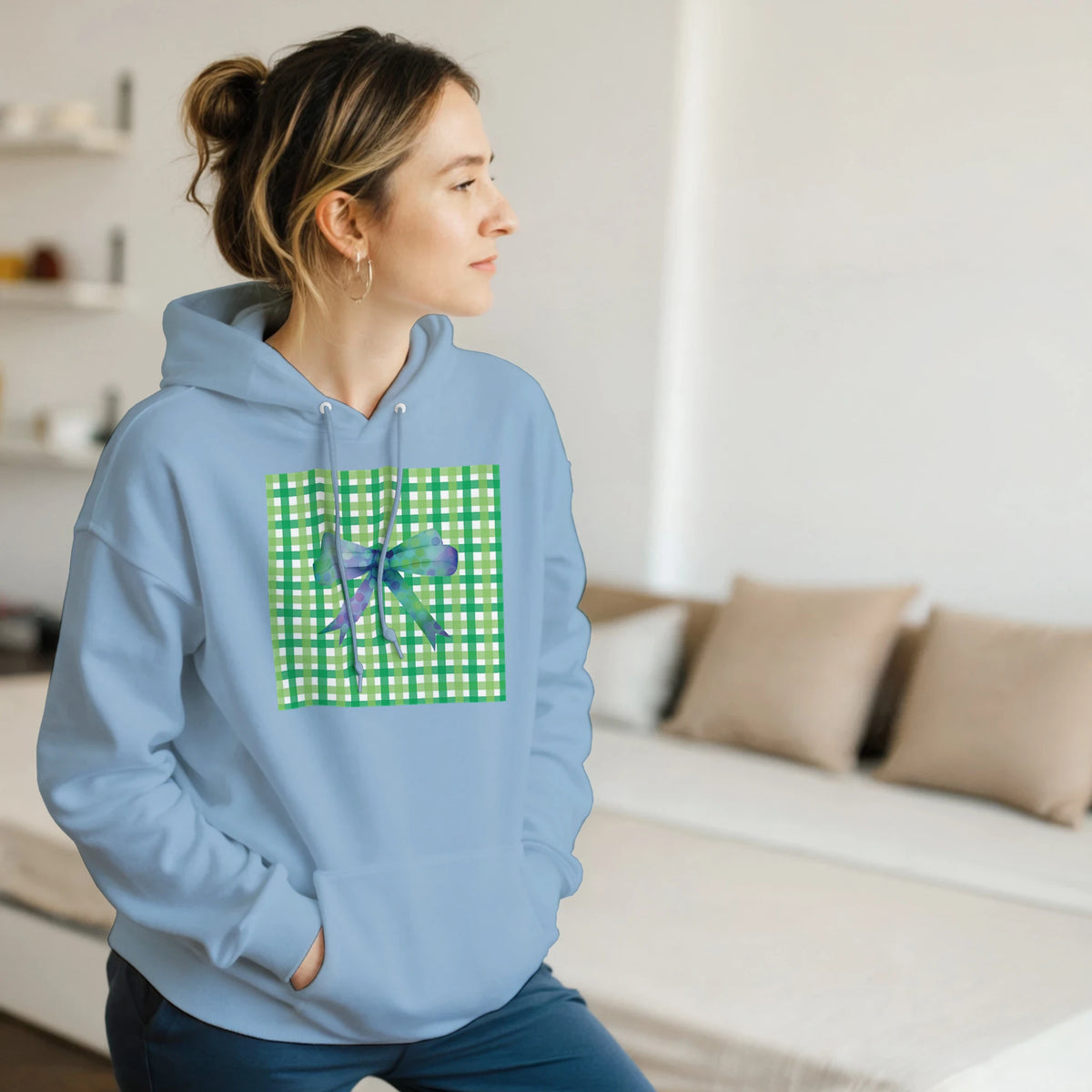 Side-profile of a woman in a light blue hoodie with a green gingham chest panel and bow.