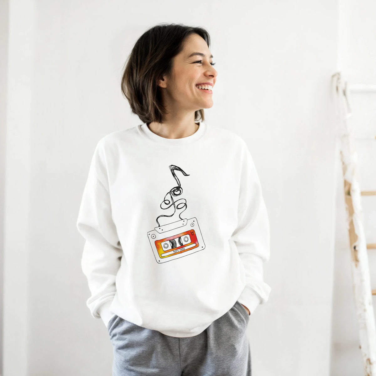 Smiling woman wearing a white Retro Cassette Tape sweatshirt with a vintage cassette graphic