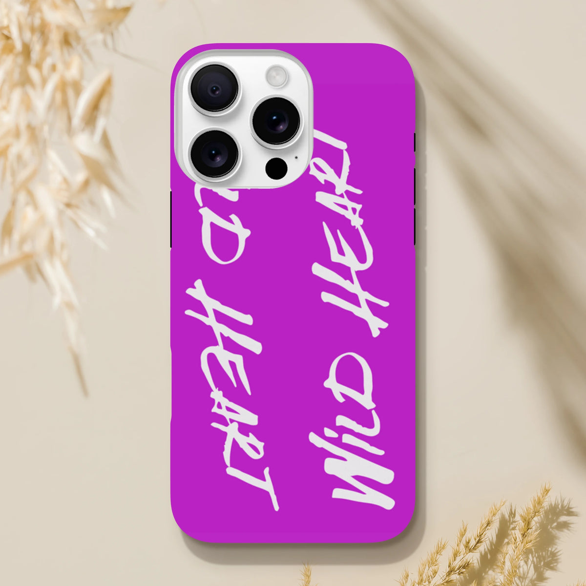 Vibrant purple iPhone case with white "Wild Heart" graffiti typography. Tough phone cover with streetwear aesthetic and shock-absorbing protection for urban style.