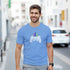 Man wearing light blue retro gamer T-shirt with pixel-art controller and skyline graphic.