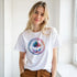 Woman wearing white retro palm tree T-shirt with a colorful circular palm tree graphic.