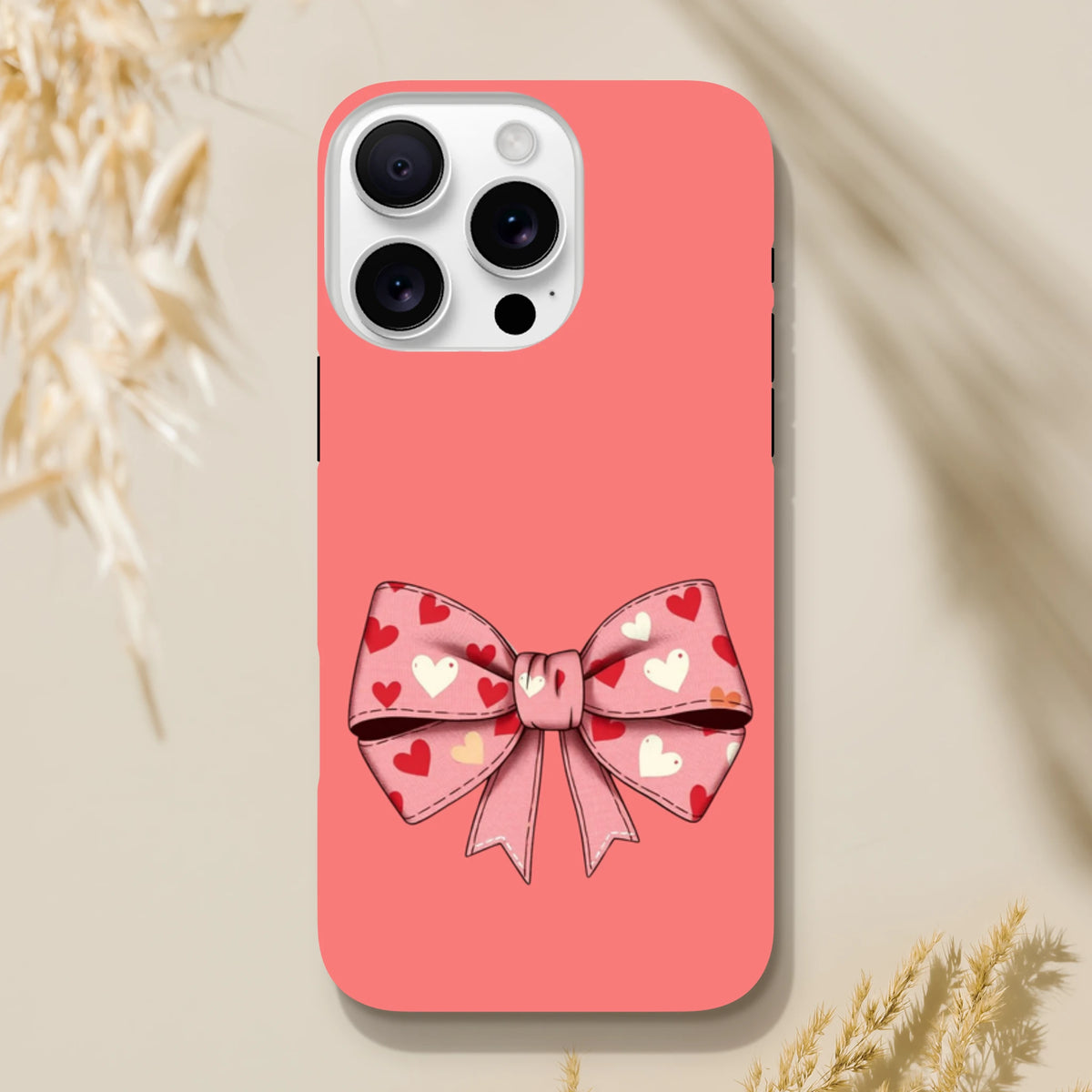Pink iPhone case featuring a large bow patterned with red and white hearts on a coral background. Cute coquette tough phone cover.
