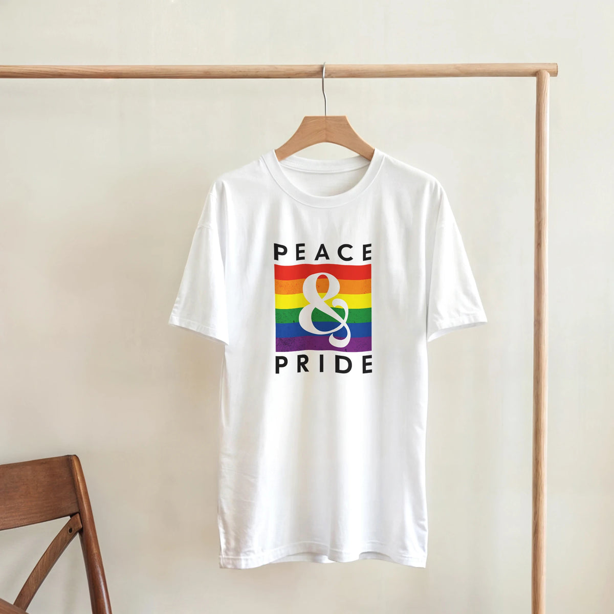 White retro tee featuring "PEACE & PRIDE" text over a vintage rainbow graphic hanging on a wooden rack.