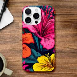 Vibrant tropical hibiscus iPhone case featuring bold pink, orange, and yellow florals with dark foliage on a wooden desk.