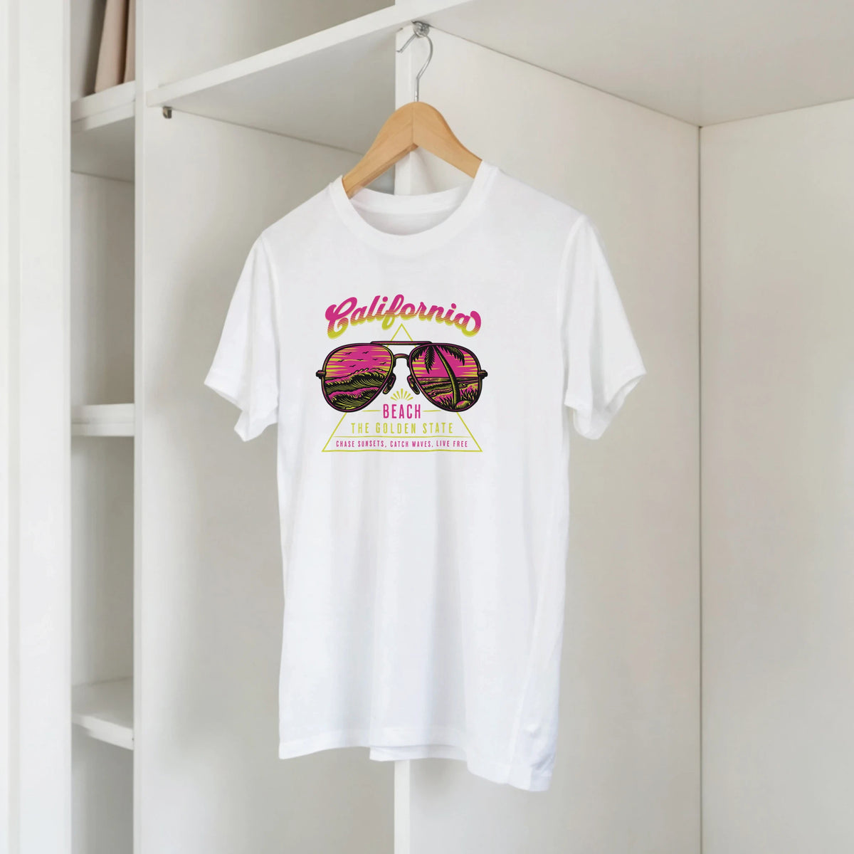 White women's T-shirt on a hanger with colorful retro California beach graphic.